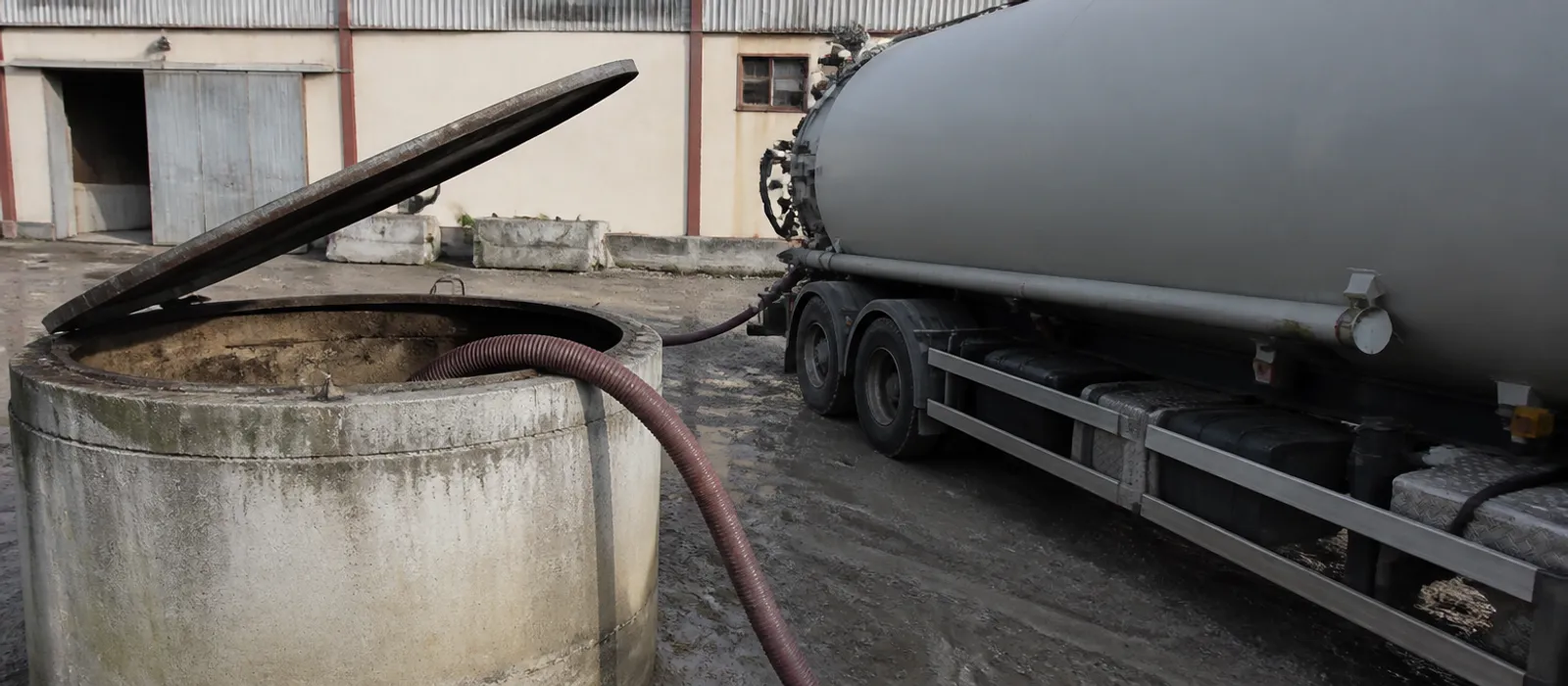 Depósito industrial abierto con manguera de aspiración de lodos y cisterna sin rotular en el patio de una nave