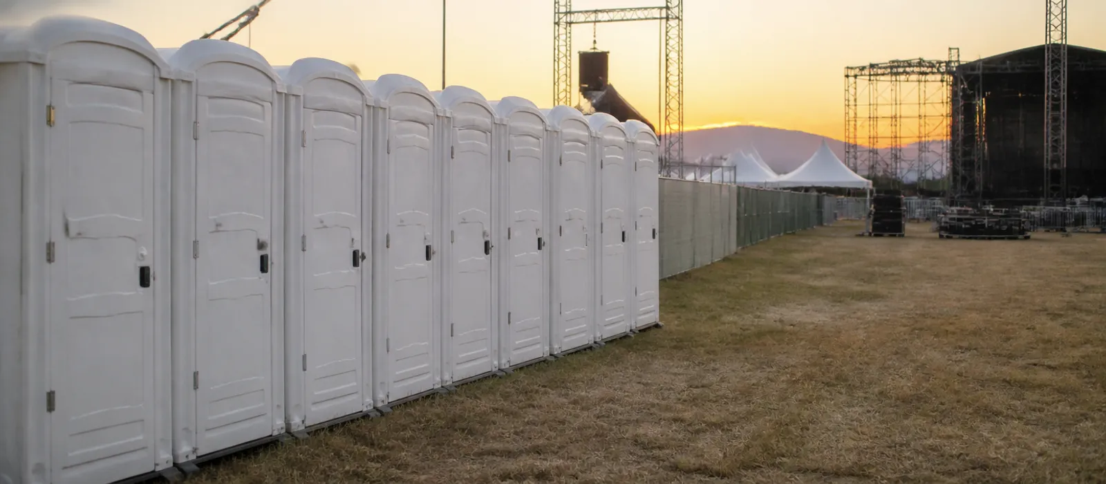 Batería de baños portátiles alineada en el lateral del recinto de un festival al aire libre