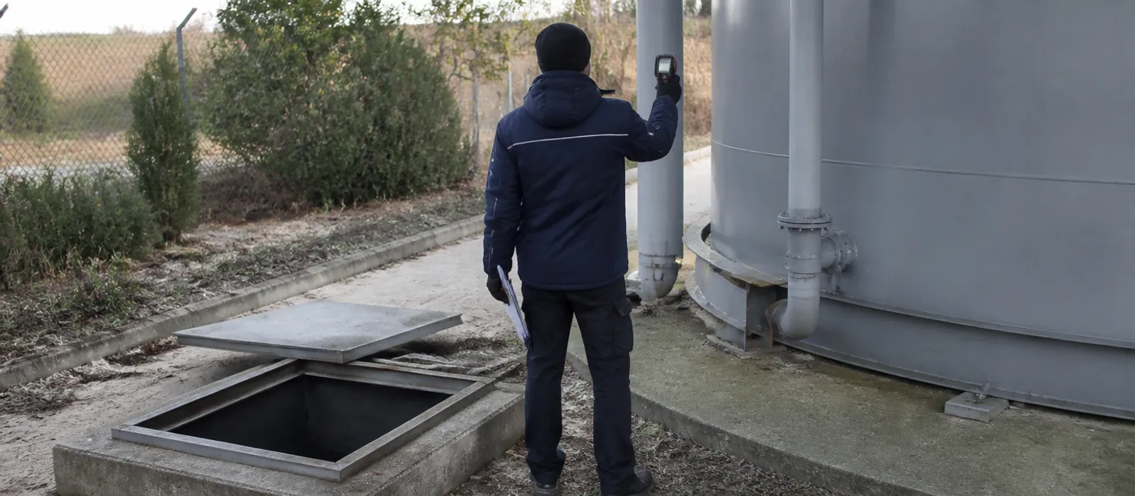 Técnico de espaldas tomando medidas junto a un depósito y una arqueta para preparar un presupuesto