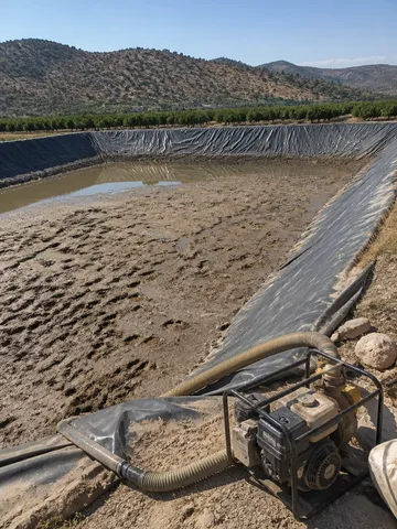 Balsa de riego vaciada con lodo en el fondo y bomba de achique en el talud