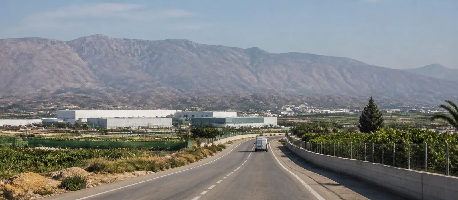 Carretera entre campos de regadío y naves industriales en la zona de servicio de Sanevanta